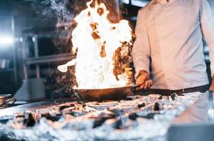 frituren pan is Aan brand. chef in wit uniform Koken voedsel Bij keuken. bezig dag Bij werk foto