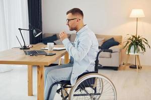 werken door gebruik makend van laptop. gehandicapt Mens in rolstoel is Bij huis foto