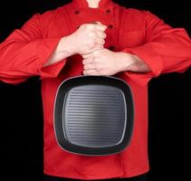 koken in rood uniform Holding een leeg plein zwart frituren pan foto