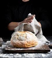 gebakken ronde brood Aan een bord achter de koken in zwart kleren foto