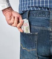 Mens in een blauw plaid overhemd en jeans zet papier Amerikaans dollars in zijn terug zak- foto