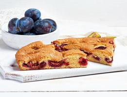 plakjes van biscuit Pruim taart Aan een wit houten bord en vers fruit foto