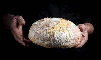 mannetje chef handen houden een geheel brood van gebakken ronde brood foto