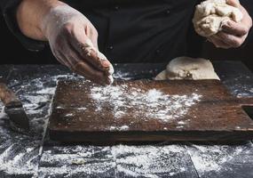 chef in zwart jasje, kneedt deeg gemaakt van wit tarwe meel foto