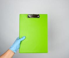 vrouw hand- met blauw medisch handschoen Holding een groen tablet voor klemmen papieren foto