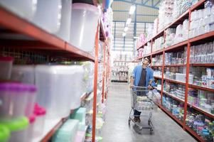 Aziatisch Mens winkelen. knap glimlachen jong Mens boodschappen doen voor huishouden items met supermarkt en boodschappen doen kar. foto