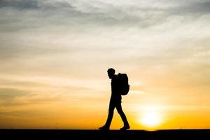 silhouet van een jonge backpackermens die tijdens zonsondergang loopt foto