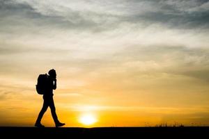 silhouet van een jonge backpackermens die tijdens zonsondergang loopt foto