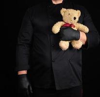 Mens in een zwart uniform houdt in zijn hand- een speelgoed- teddy beer foto