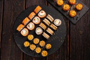 groot sushi reeks van top Aan zwart achtergrond. een assortiment van divers maki nigiri en broodjes zeevruchten soja saus foto