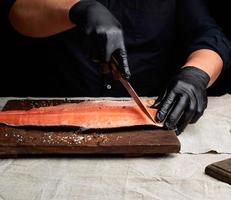 chef in zwart kleren en zwart latex handschoenen bezuinigingen vers Zalm filet in stukken foto