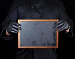chef in zwart uniform en zwart latex handschoenen houdt een leeg houten kader foto