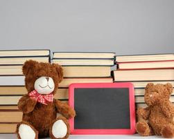 bruin teddy beer en leeg zwart bord in rood kader Aan de achtergrond van stapel van boeken foto