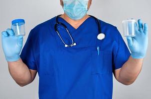 dokter in blauw uniform en latex handschoenen is Holding een leeg plastic houder voor nemen urine monsters foto