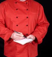 chef in rood uniform Holding een blanco notitieboekje en een zwart houten potlood foto