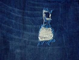 fragment van blauw jeans kleding stof met een gat, vol kader foto