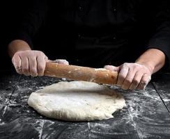 chef in een zwart tuniek broodjes een deeg voor een ronde pizza foto
