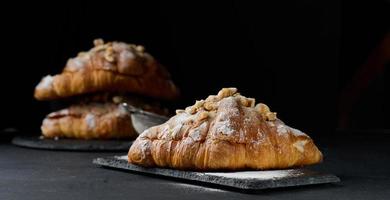 gebakken croissant Aan een houten bord en besprenkeld met gepoederd suiker, zwart tafel. smakelijk gebakjes voor ontbijt foto