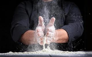 chef in zwart uniform giet wit tarwe meel uit van zijn handen foto