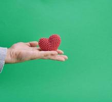 een klein gebreid rood hart in een menselijk hand- Aan een blauw achtergrond foto