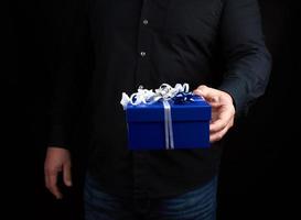 volwassen Mens in een zwart overhemd houdt een blauw plein doos met een wit boog foto