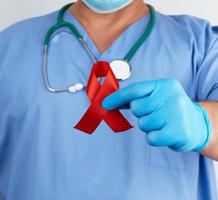 dokter in blauw uniform en steriel latex handschoenen houdt een rood lint foto