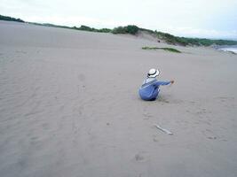 terug van de vrouw in de hoed wie was zittend en spelen strand zand, de visie van de zand foto