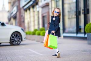 aanbiddelijk weinig meisje wandelen met boodschappen doen Tassen buitenshuis foto