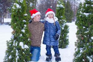 aanbiddelijk weinig meisje en gelukkig vader in de kerstman hoeden buitenshuis foto