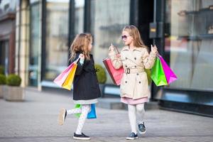 aanbiddelijk weinig meisjes Aan winkelen. portret van kinderen met boodschappen doen Tassen. foto