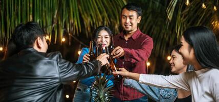 portret van gelukkig Aziatisch vrienden hebben avondeten partij samen - jong mensen zittend Bij bar tafel roosteren bier bril avondeten buitenshuis - mensen, voedsel, drinken levensstijl, nieuw jaar viering concept. foto