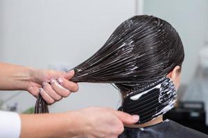 kapper is van toepassing een haar- masker naar Rechtdoor zwart haar. haar- zorg Bij de schoonheid salon. foto