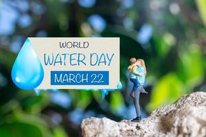 miniatuur mensen moeder Holding zoon in de armen en woorden geschreven Aan papier wereld water dag foto