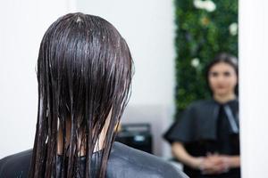 kapper is van toepassing een haar- masker naar Rechtdoor zwart haar. haar- zorg Bij de schoonheid salon. foto