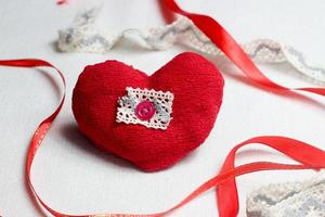 hand- gemaakt rood hart dichtbij omhoog Aan licht achtergrond met rood lint, Valentijn dag ansichtkaart, vakantie behang, dekking: ontwerp, handwerk hobby. foto