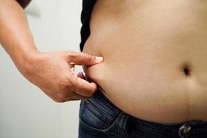 overgewicht aziatische vrouw gebruikt hand om dikke buik te knijpen groot formaat overgewicht en obesitas. foto