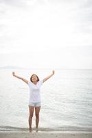jonge mooie vrouw strekt haar armen in de lucht op het strand met blote voeten foto