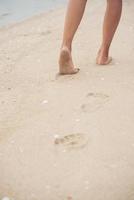 jonge vrouw lopen op zand strand voetafdrukken achterlatend foto