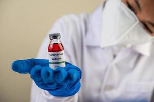 een wetenschapper met masker en handschoenen draagt flesjes met vaccins ter bescherming tegen covid-19