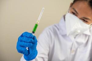 wetenschapper die beschermende maskers draagt en handschoenen die een injectiespuit met een vaccin vasthouden om covid-19 te voorkomen