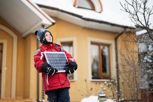 jongen met zonne- paneel tegen huis in winter. alternatief energie concept. foto