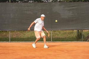 senior tennis speler gekleed in sportkleding in actie Aan een klei tennis rechtbank foto