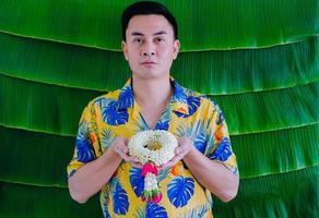 Thais Mens Holding jasmijn slinger naar geven zegen voor songkran festival met banaan blad achtergrond. foto