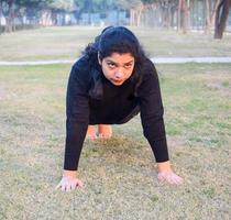 jong Indisch vrouw beoefenen yoga buitenshuis in een park. mooi meisje praktijk eenvoudig yoga houding. rust en kom tot rust, vrouw geluk. eenvoudig yoga poses buitenshuis foto