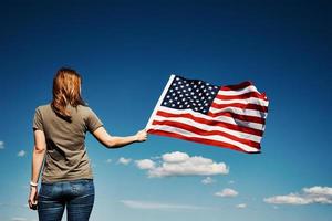 vrouw houdt Verenigde Staten van Amerika vlag tegen blauw lucht foto