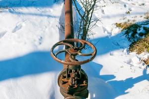 roestig oud gas- kraan Aan een achtergrond van wit sneeuw in winter. foto