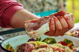 een kom gevulde met gemarineerd rauw vlees en vrouwen handen rijgen kebab Aan een vleespen foto