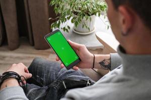 een jong vent is op zoek Bij een telefoon scherm met een chroom sleutel binnenshuis. persoon gebruik makend van smartphone met groen scherm foto