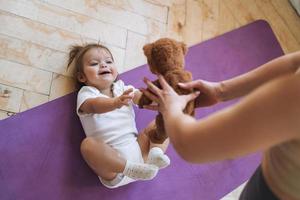 jong vrouw fit mam met baby meisje aan het doen geschiktheid Aan mat Bij huis foto