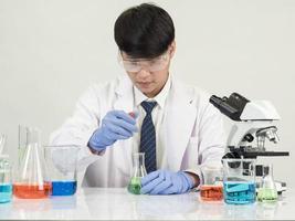 Aziatisch mannetje leerling wetenschapper in reagens menging laboratorium in een wetenschap Onderzoek laboratorium met test buizen van divers maten en microscopen. Aan de tafel in laboratorium chemie laboratorium wit achtergrond. foto